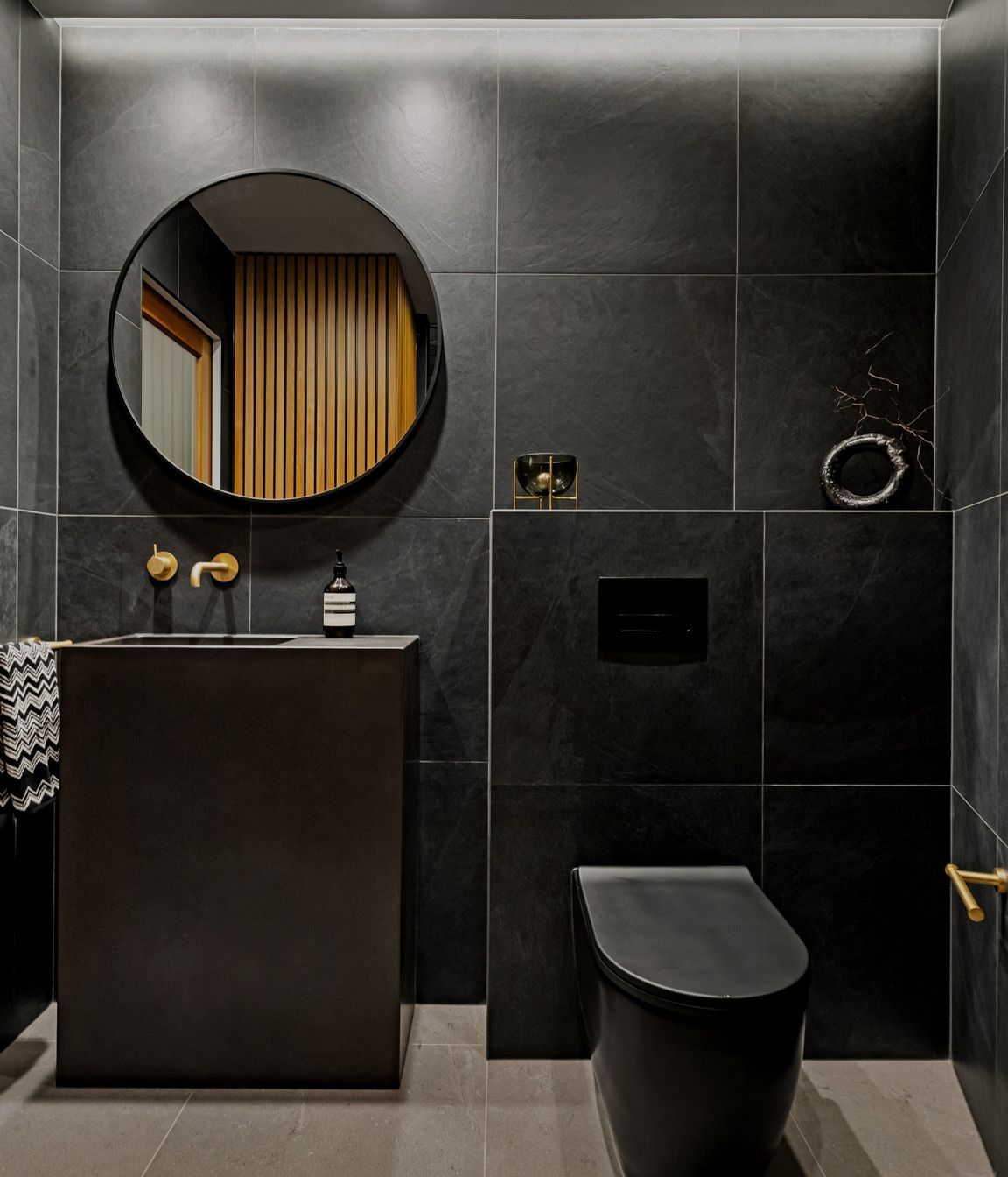 A refined color palette showcases aged brass Progetto tapware alongside elegant imported Italian black tiles and toilet, creating a sophisticated and cohesive aesthetic throughout the space.