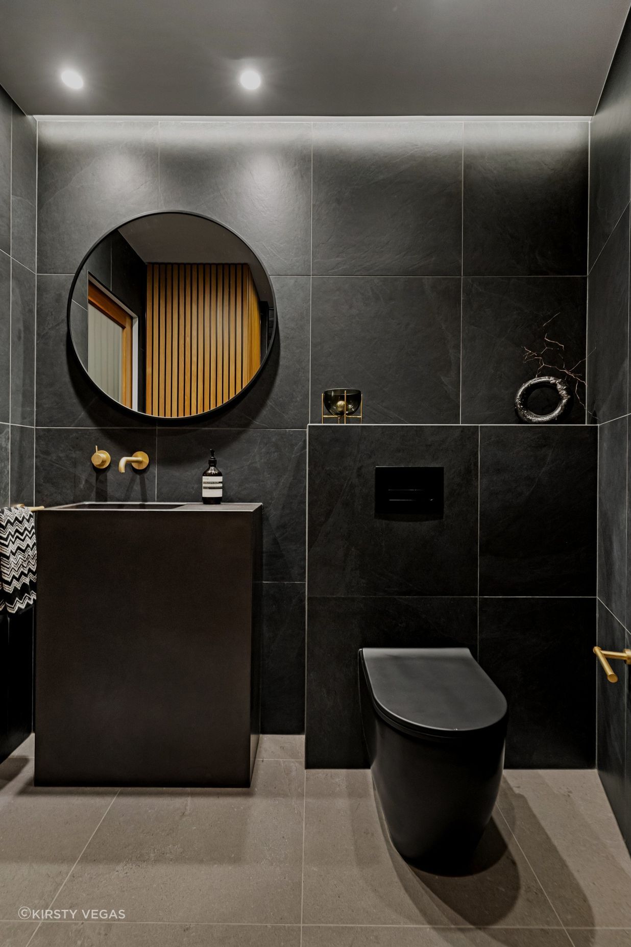 A refined color palette showcases aged brass Progetto tapware alongside elegant imported Italian black tiles and toilet, creating a sophisticated and cohesive aesthetic throughout the space.