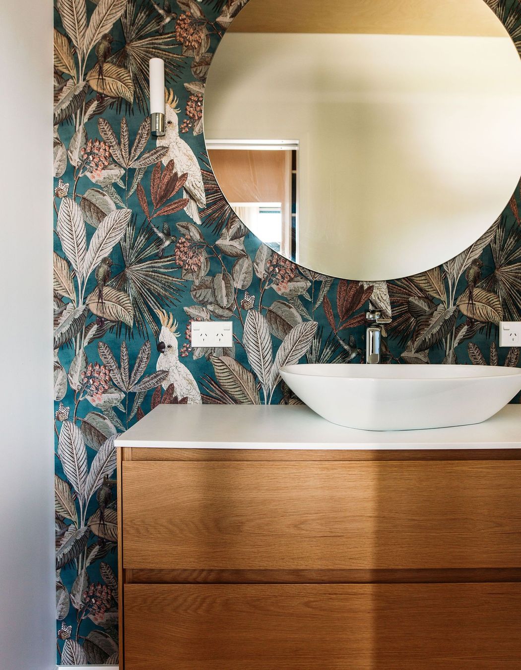 A beautiful oak 2-drawer vanity is framed by the wonderful wallpaper.