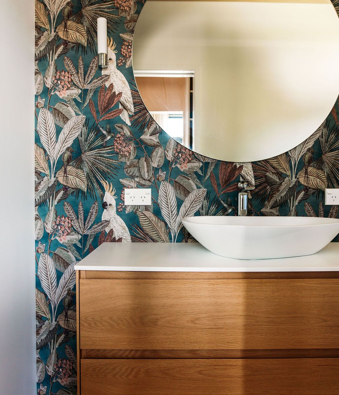A beautiful oak 2-drawer vanity is framed by the wonderful wallpaper.