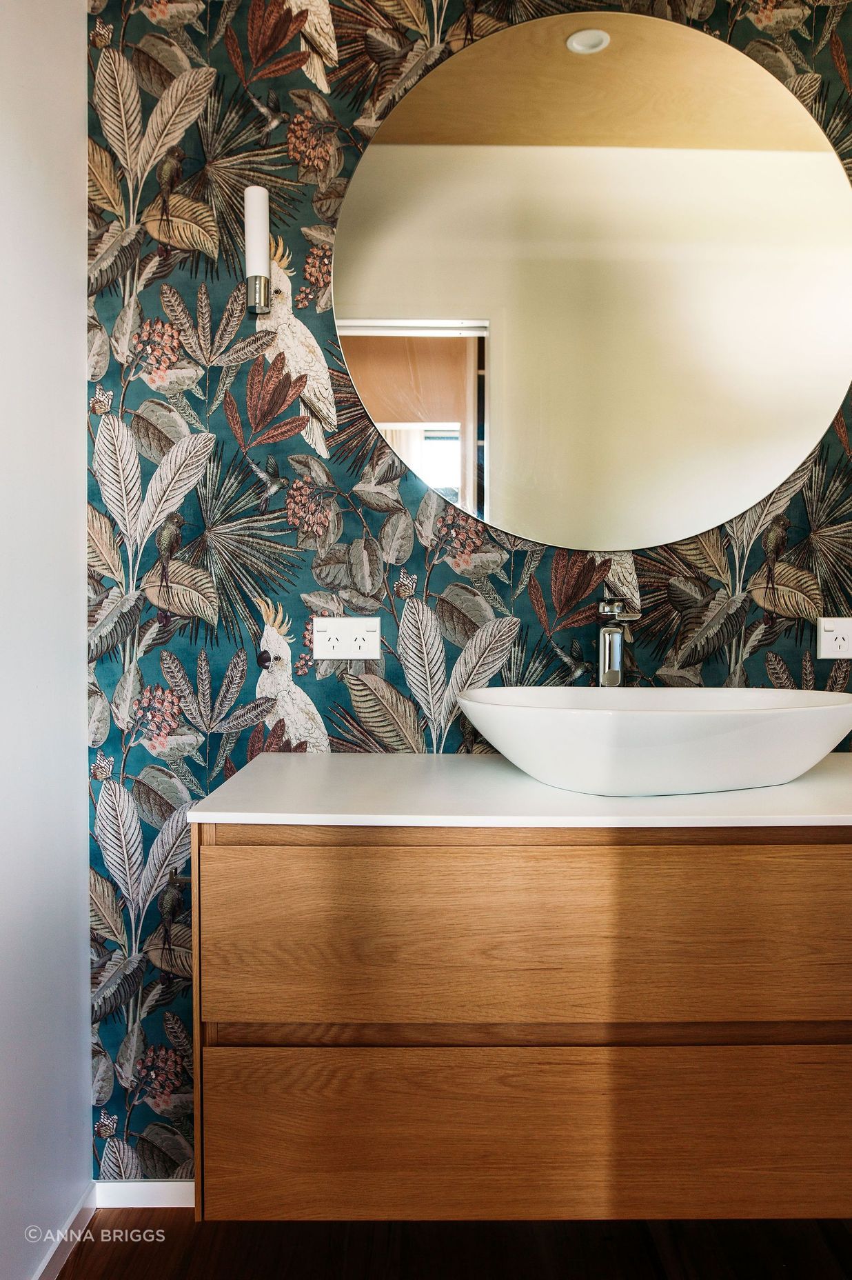 A beautiful oak 2-drawer vanity is framed by the wonderful wallpaper.