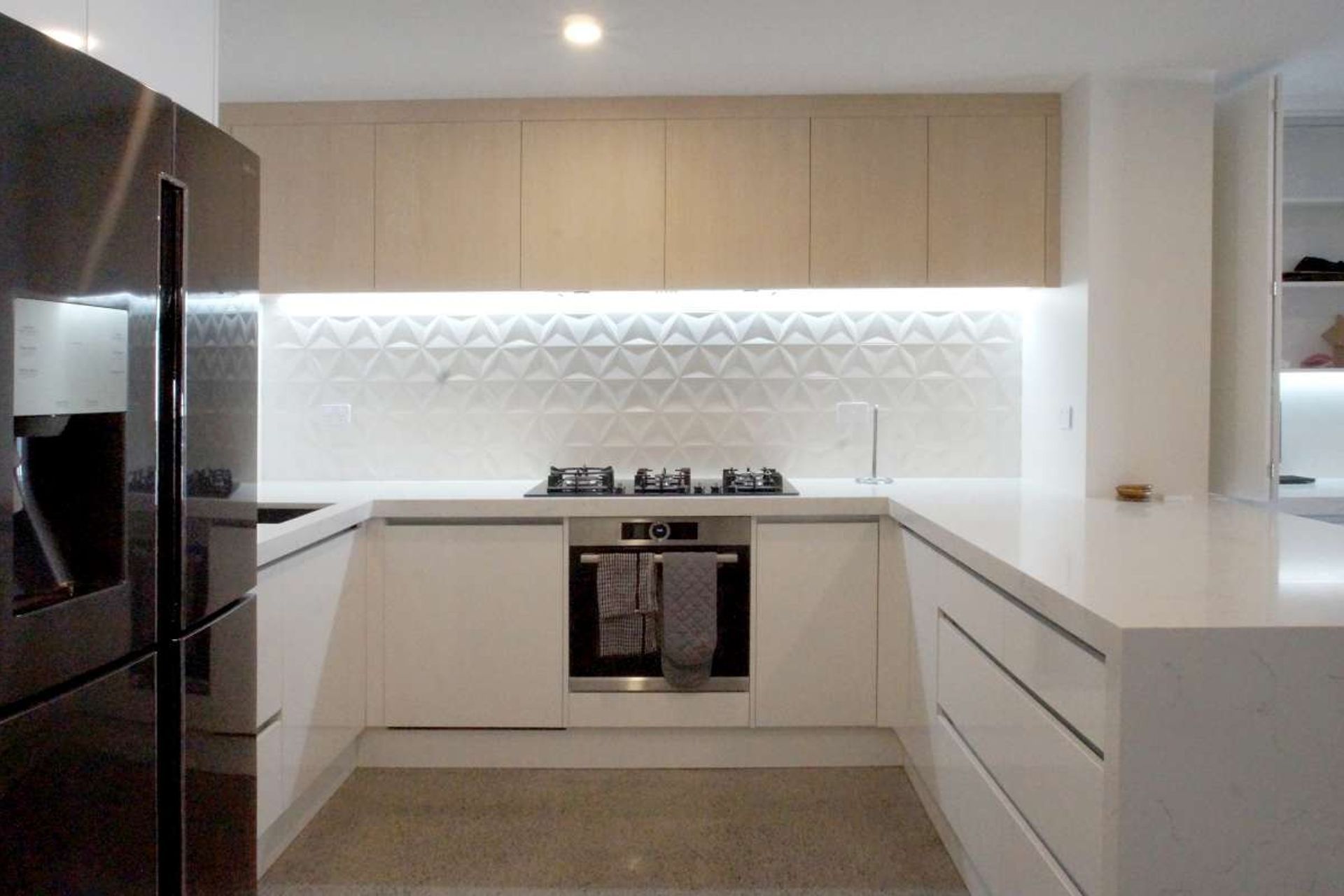 Kitchen renovation in Parnell. Concrete Floors, textured 3D hexagonal white backsplash, hot water tap sink, marble look stone engineered benchtop, LED lights on 'no handle' drawer set up