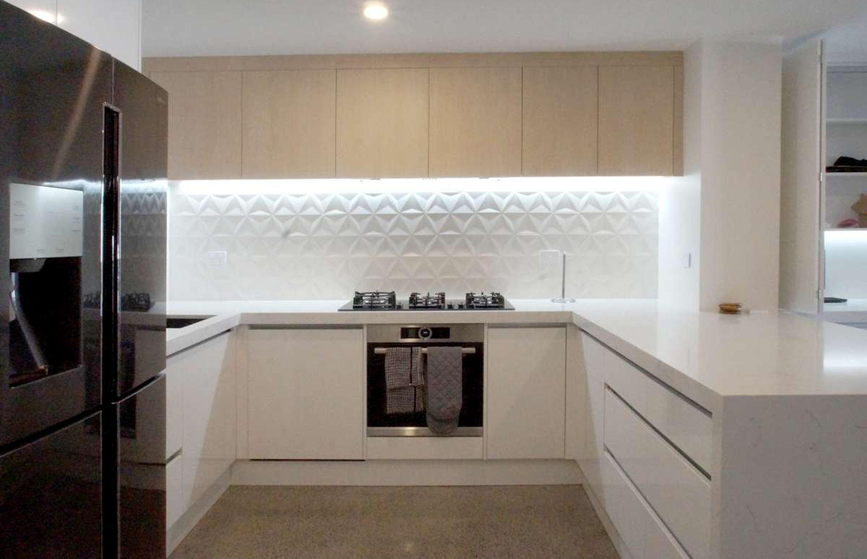 Kitchen renovation in Parnell. Concrete Floors, textured 3D hexagonal white backsplash, hot water tap sink, marble look stone engineered benchtop, LED lights on 'no handle' drawer set up
