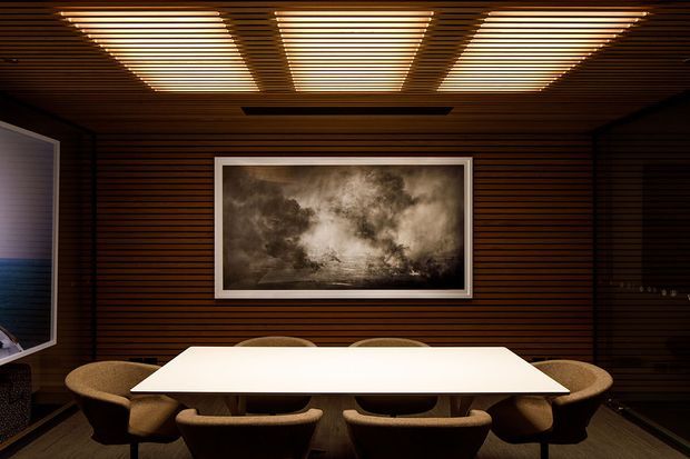 Dark, refined dining or meeting room with extensive horizontal dark timber wall and ceiling panelling, a large white rectangular table, upholstered chairs, integrated linear ceiling lighting, and a framed monochrome artwork.