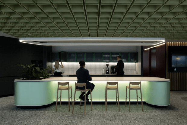 Contemporary commercial hospitality or workplace lounge with a long curved illuminated counter and integrated seating. The space features a dark palette, pale illuminated counter front, tiled back counter with coffee equipment, timber stools, indoor planting, and a distinctive exposed square-grid ceiling with a large suspended linear light.