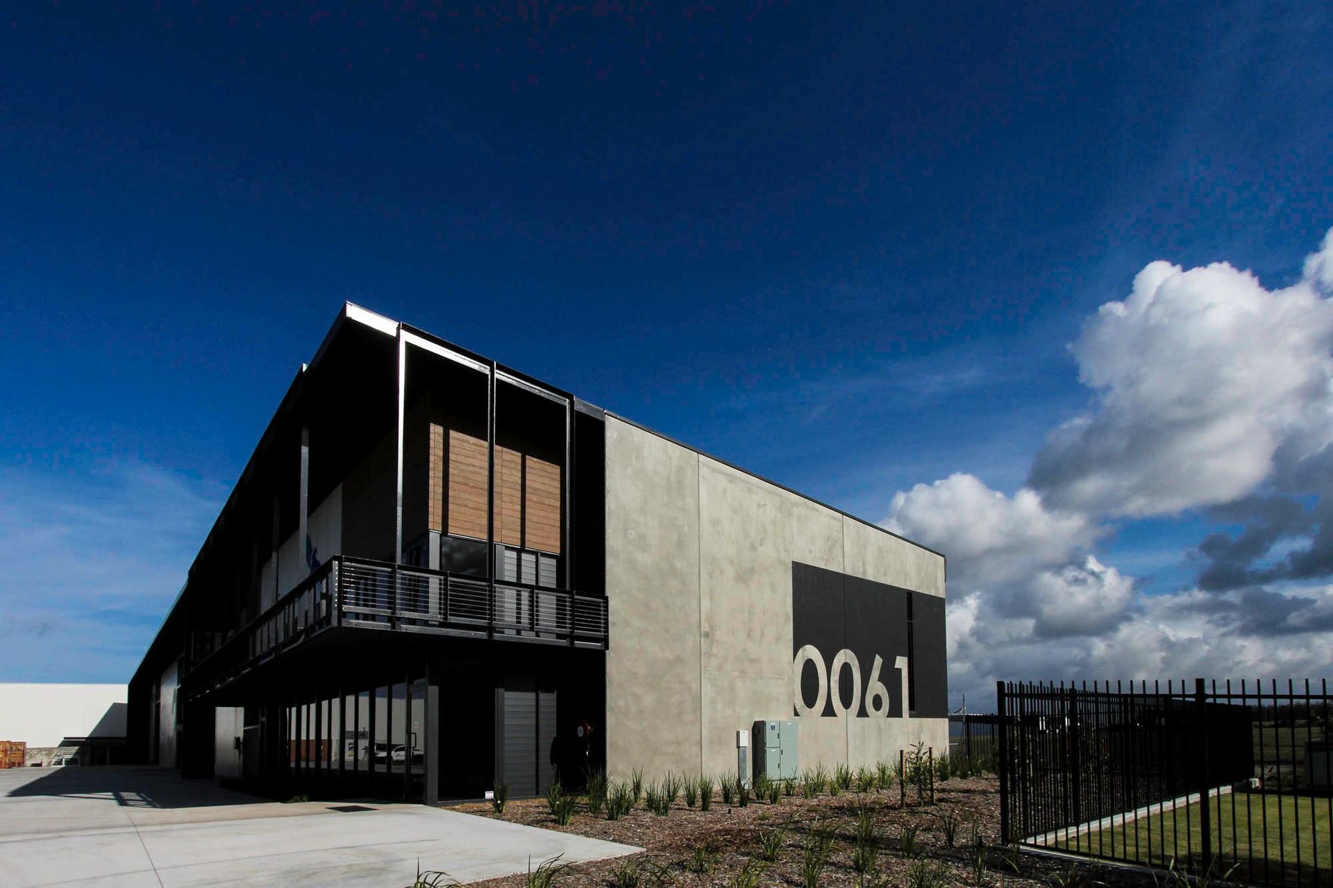 Eniquest Warehouse - Exterior. Office pavilion and concrete warehouse against a blue sky.