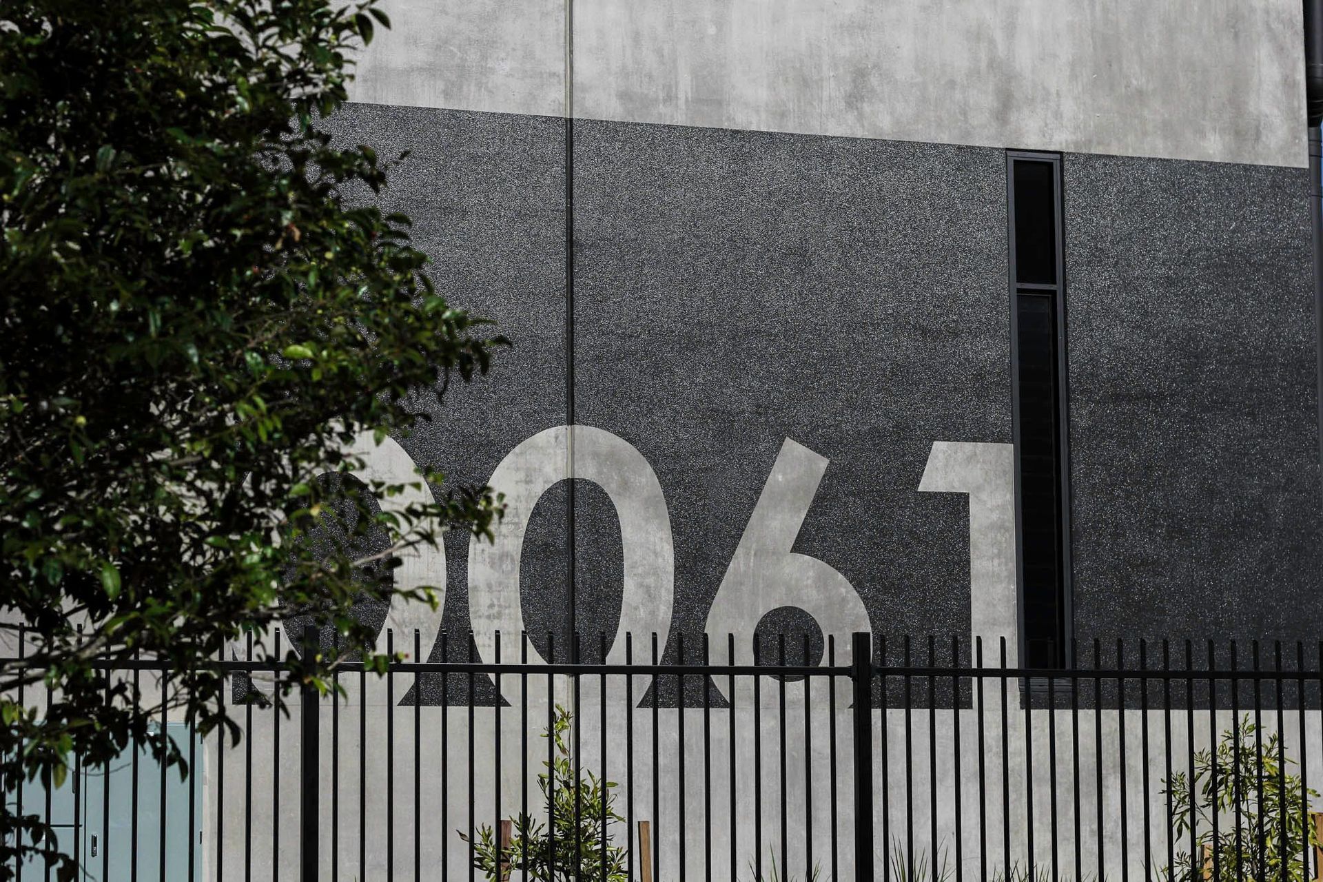 Eniquest Warehouse - Exterior. Building number on dark cladding behind native planting.