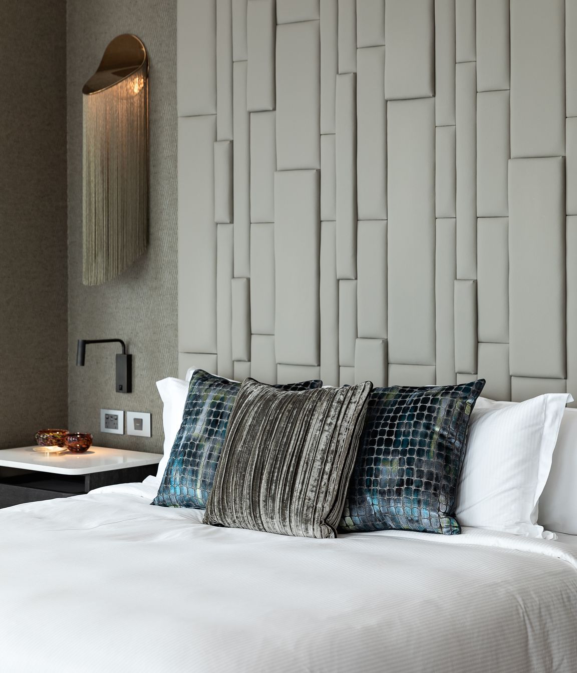 A textured padded headboard makes a grand statement alongside the incredible wall lamp.