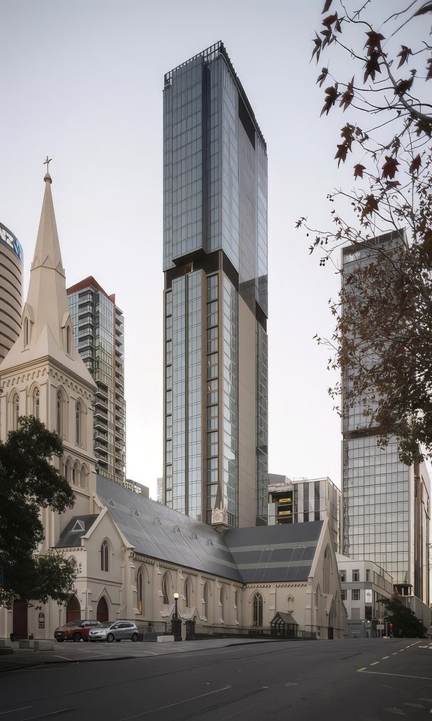 Street-level urban exterior view of a historic Gothic Revival church with a tall pointed spire in the foreground, surrounded by contemporary high-rise office or apartment buildings with extensive glazed curtain walls. The scene shows a dense city setting and a strong contrast between heritage masonry architecture and modern glass towers.