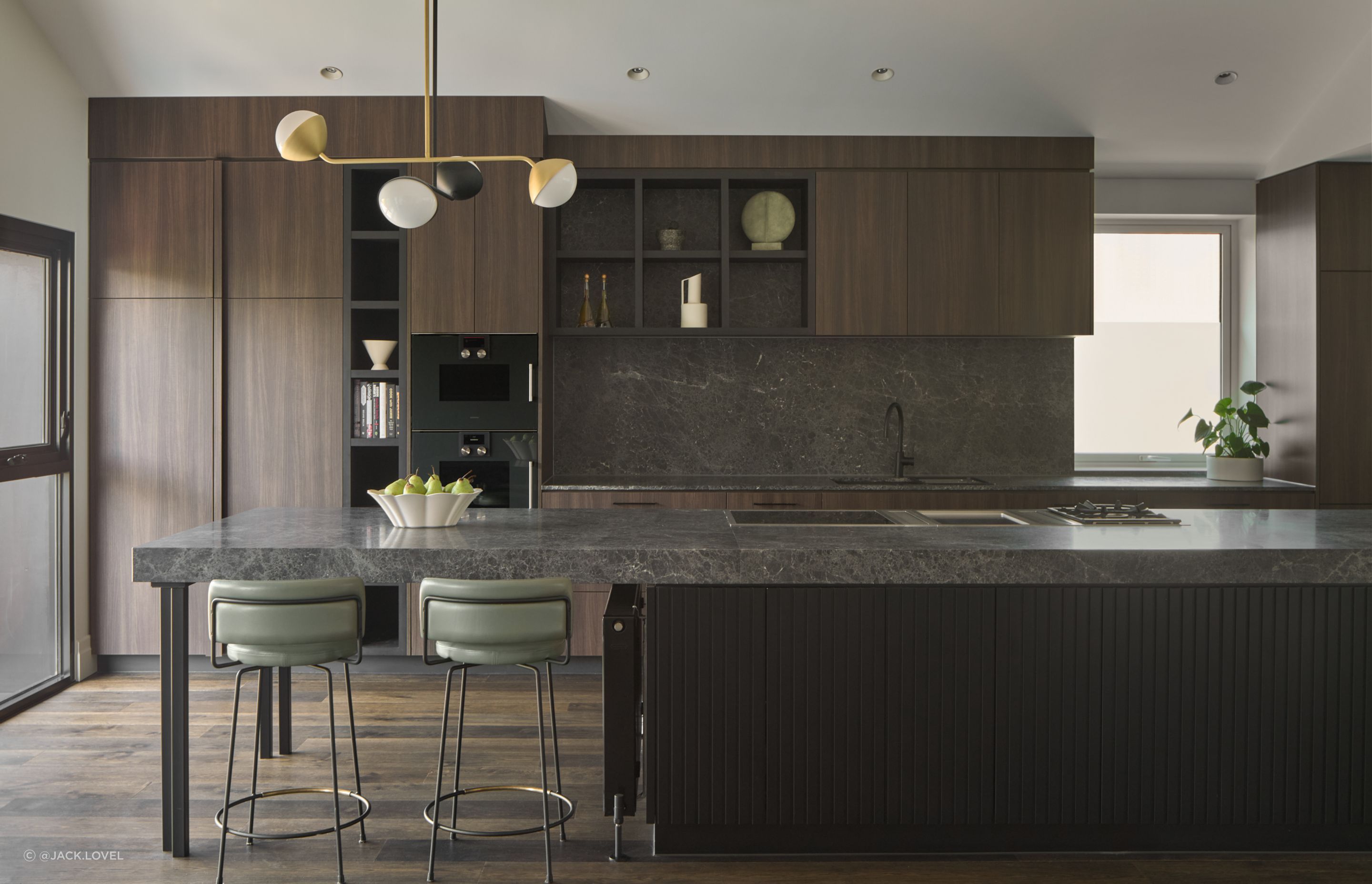 At the heart of the home, the kitchen is a study in both form and function. An expansive island anchors the space, with custom seating and pendant lighting adding sculptural flair. Art Deco references shine through—tailored, warm, and wonderfully livable.