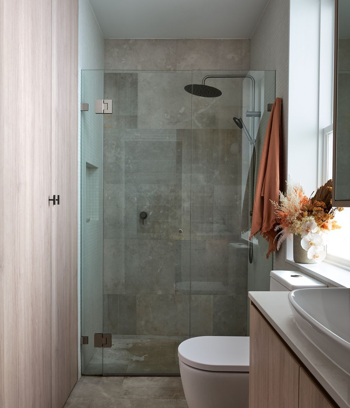 The shared bathroom takes advantage of its location and access to preinstalled services. Sharing footprint, the space underneath the stairs is further utilised as laundry, and storage space, concealed behind seamless joinery accessed through the bathroom.