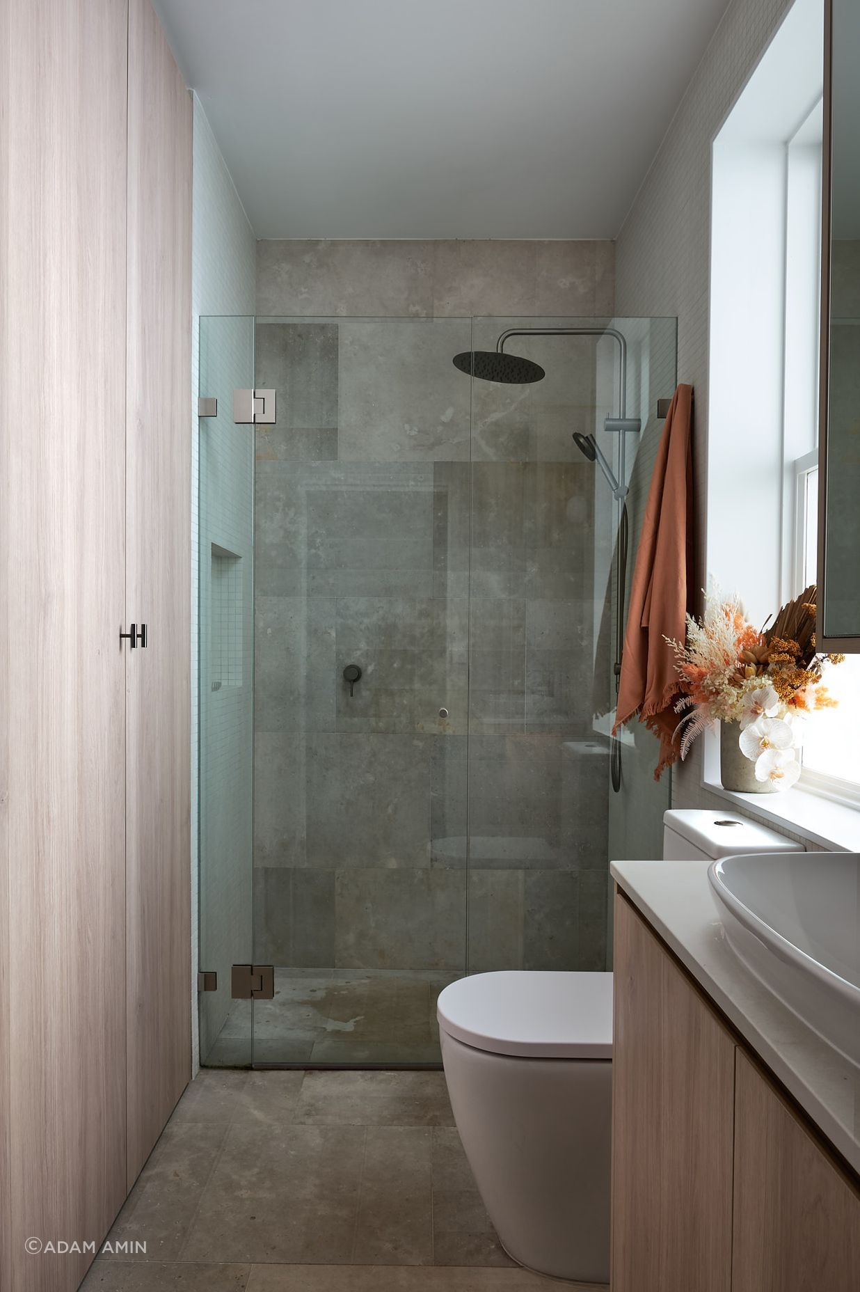 The shared bathroom takes advantage of its location and access to preinstalled services. Sharing footprint, the space underneath the stairs is further utilised as laundry, and storage space, concealed behind seamless joinery accessed through the bathroom.