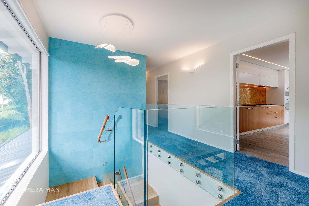 The feature wallpaper is Elitis Wallpaper Natives Maori. It runs floor to ceiling over two stories. The wallpaper reflects Oceania. The Diphy_P3 Pendant by Grok looks like sea creatures swaying and floating and the wing lights in the hall evoke sea birds hovering above the ocean.