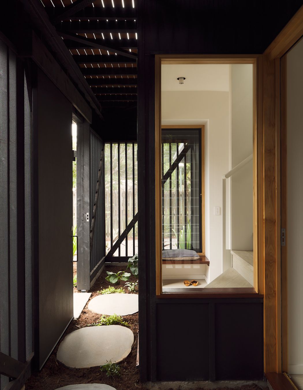 Gentle natural light filters through a timber screened outdoor space, creating a calm and breezy undercroft entry to this inner-city cottage.