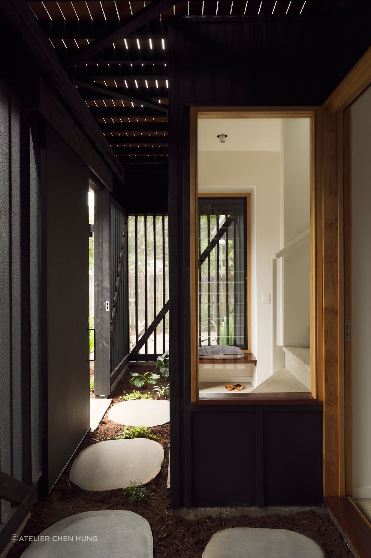 Gentle natural light filters through a timber screened outdoor space, creating a calm and breezy undercroft entry to this inner-city cottage.