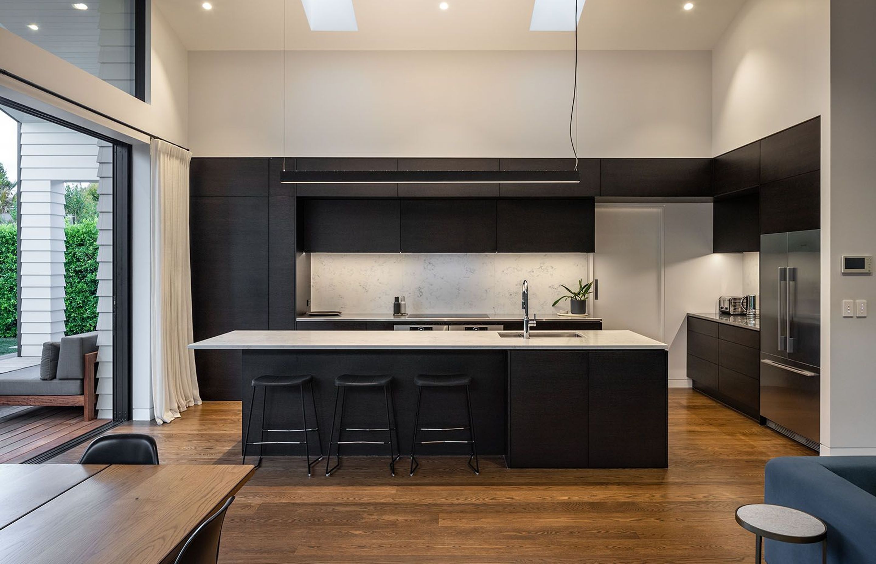 Dark tones were chosen for the kitchen cabinetry to help the space recede into the background. Behind the white cavity slider on the right is the scullery. The large 'cabinet' to the left is actually a doorway to the laundry and garage.