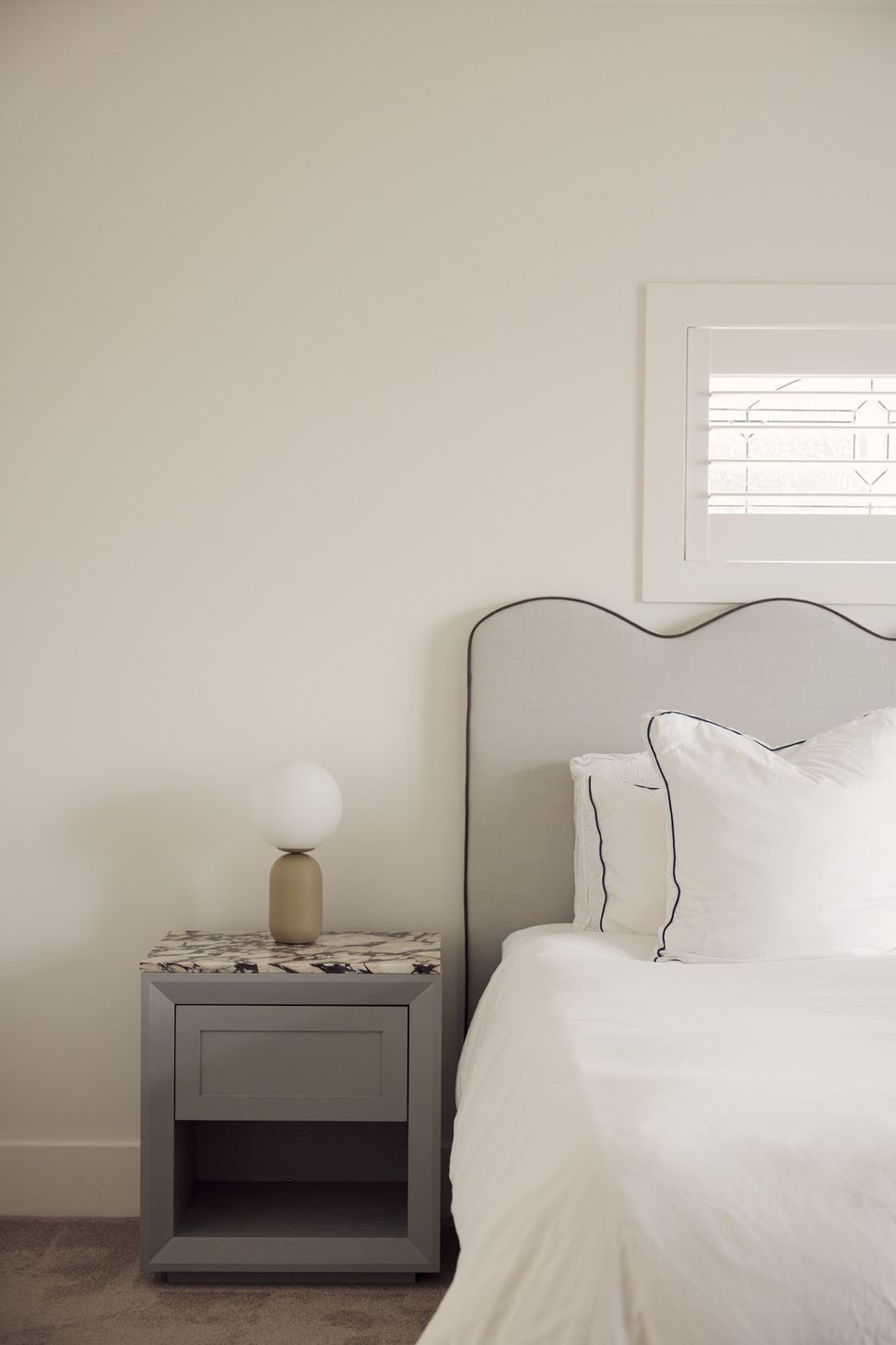 Scalloped bedhead, marble-topped bedside and the original leadlight window retained as a quiet feature — bedroom detail at Point Chevalier Bungalow. In collaboration with Hannah Warren Interiors.