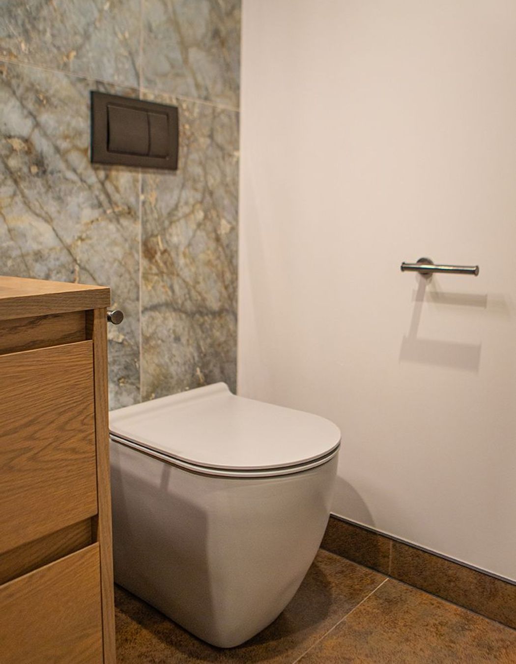 Slimline toilet with in-wall cistern and aged iron mechanical flush plate.