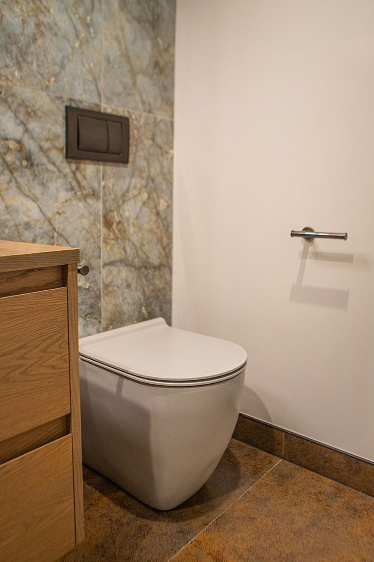 Slimline toilet with in-wall cistern and aged iron mechanical flush plate.