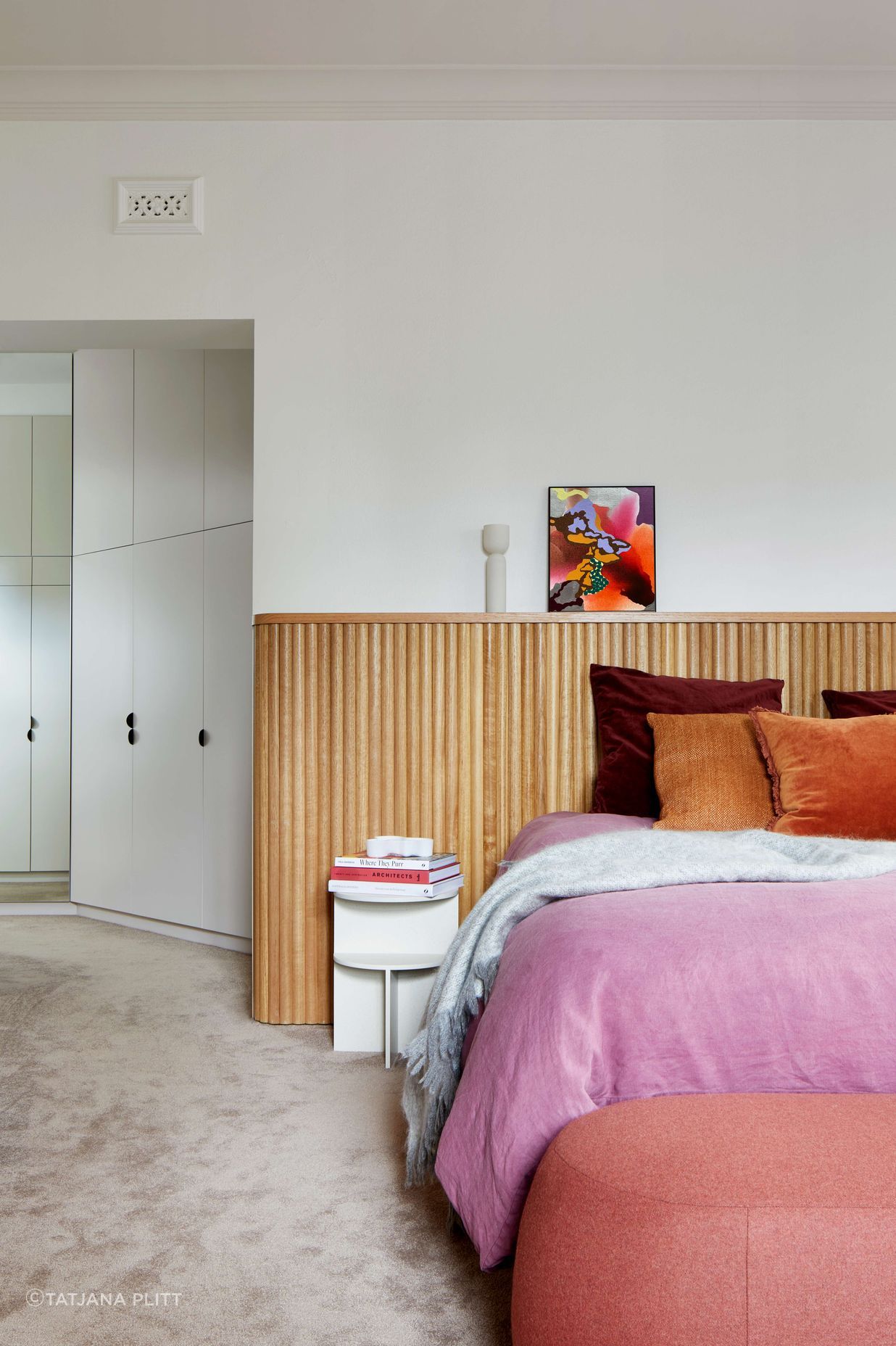 Master bedroom with headboard created with tasmanian oak wood dowels for a highly finished art deco minimalist feel. Cushions and bedding provide pops of colour in warm pink and jeweled colour oranges and burgundies. Pale pink  coloured carpet from Edel Carpets. Home located in Melbourne. See more from our Arch Deco Project.