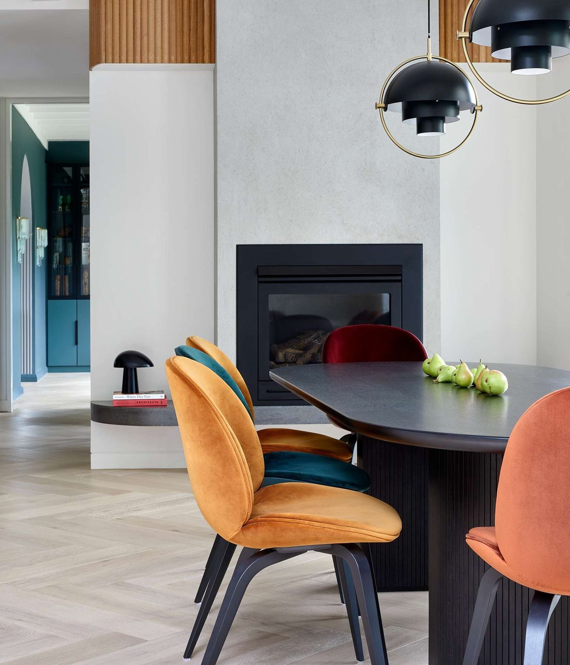 Modern inspired dining room with pops of colour from jewel coloured chairs to play off the art deco heritage of the home. The dining chairs are upholstered beetle dining chairs from Gubi, as is the elliptical shaped black dining table with bevelled half moon legs which reference simple design curves from the art deco period. Overhanging art deco inspired black and brass pendant lights are from Gubi. The flooring is in pale oak in a herringbone pattern from Havwoods, another nod to the art deco period of the home. Located in Melbourne, see more from our Arch Deco Project