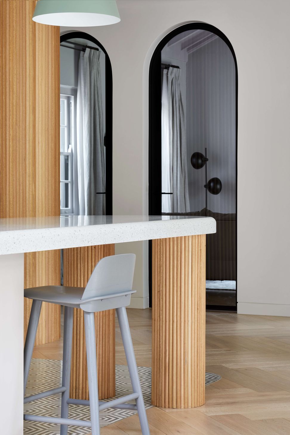Open concept kitchen with soft pastel coloured finishes featuring cool grey cement hexagon patterned tiles on the floor,  silver birch coloured corian stone bench top and hand crafted oversized pedestal legs using half round dowels as the finish for a contemporary and modern feel. Located in Melbourne, see more from our Arch Deco Project.