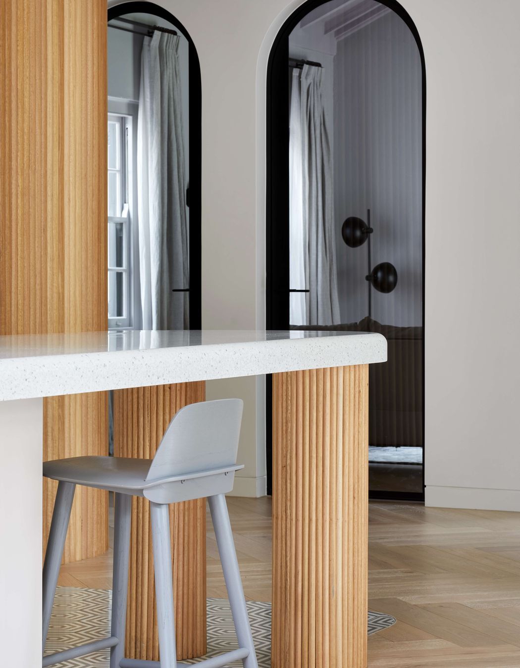 Open concept kitchen with soft pastel coloured finishes featuring cool grey cement hexagon patterned tiles on the floor,  silver birch coloured corian stone bench top and hand crafted oversized pedestal legs using half round dowels as the finish for a contemporary and modern feel. Located in Melbourne, see more from our Arch Deco Project.
