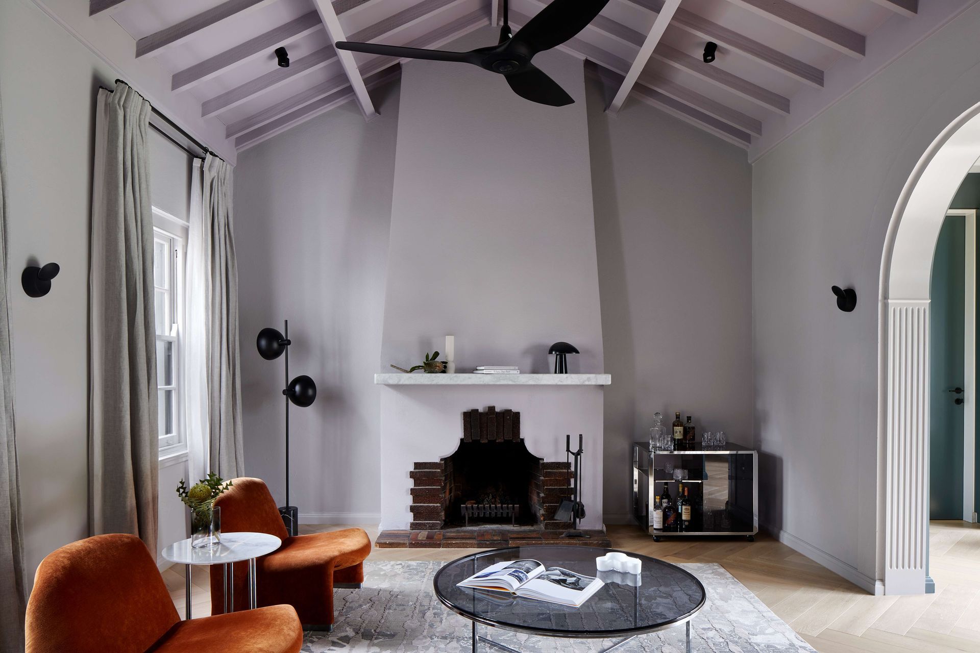 Living room with central 1930’s Art Deco original fireplace and vaulted ceiling painted in violet from Dulux. Flooring is oak with a matt lacquer to draw in the art deco heritage of the home. The room is furnished with Elke paprika velvet chairs from Castelli, and the Willy Rizzo Bar cart from Castorina. See more from our Arch Deco Project.