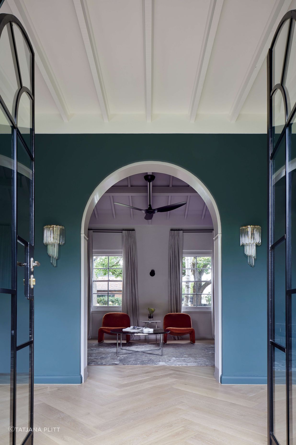 Library view from the living room through arched doorways and ceiling beams to keep with the art deco style of this house. Wall painted in dark green (Coriole) from Dulux (colour: Coriole). Crystal wall pendant lights frame the doorway and flooring is european oak laid in herringbone pattern with a matt lacquer for a minimalist styling.Project is a 1930s art deco spanish mission style house in Melbourne. See more from our Arch Deco Project.