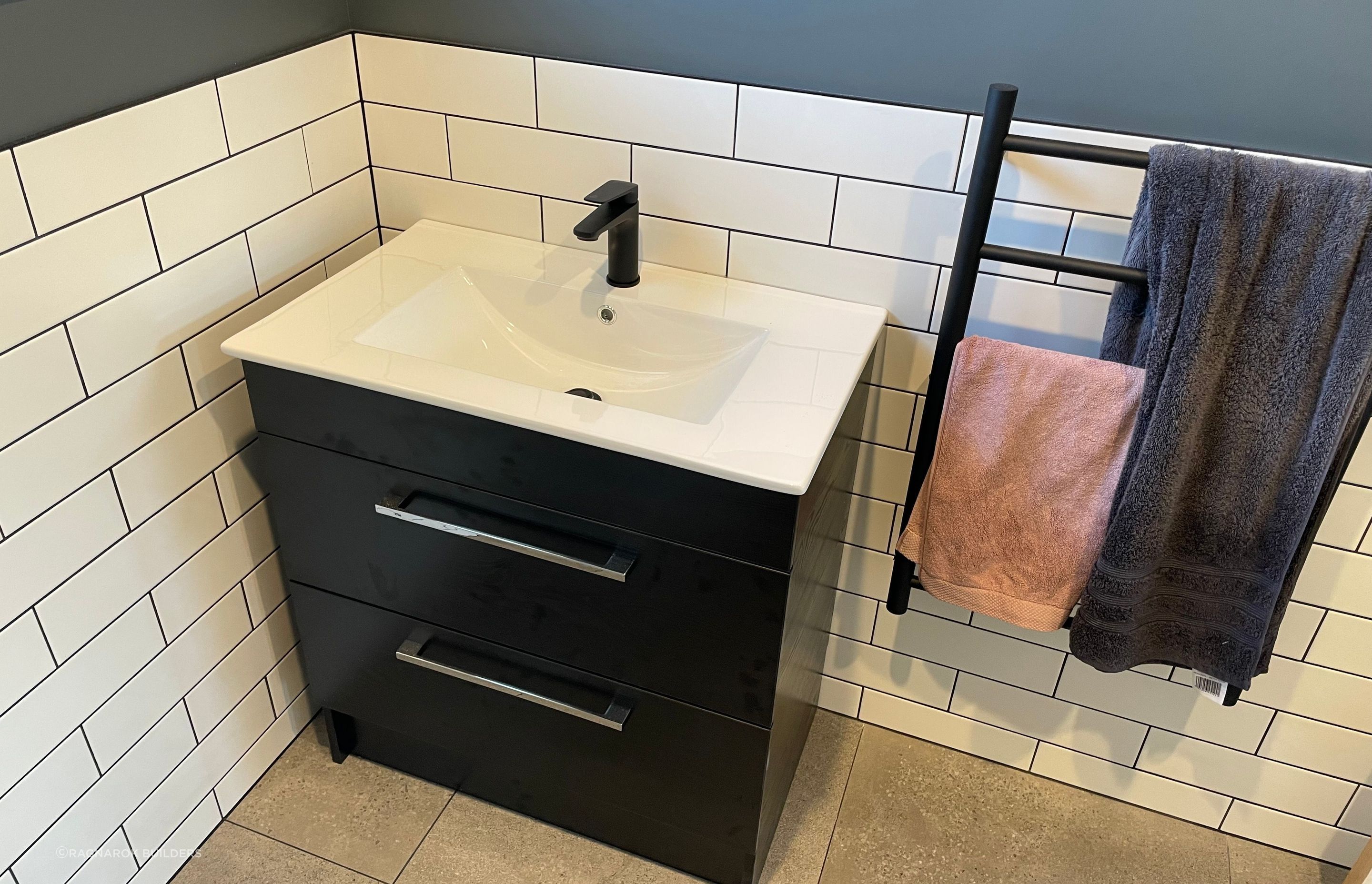 Black and white vanity with matching tiles and towel rail.
