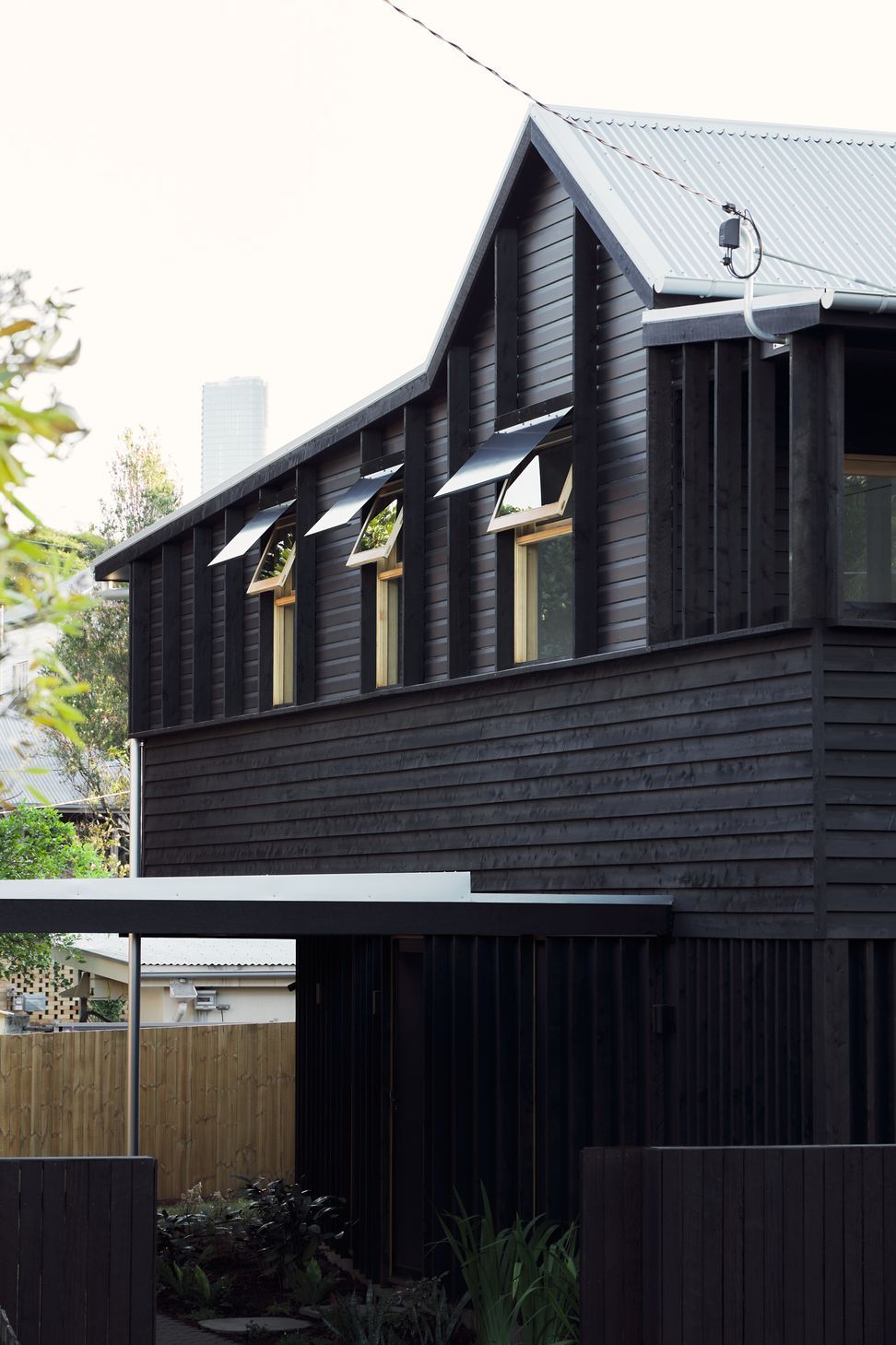 Highgate Hill Cottage’s side facade is articulated with timber studs on the existing upper band, a central horizontal band of textural weatherboard, and a lower band of vertical stud framing, unified with a transparent black stain.