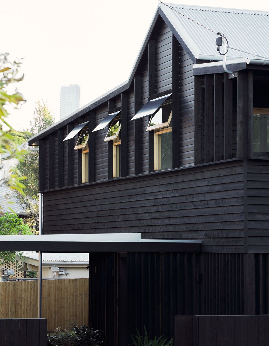 Highgate Hill Cottage’s side facade is articulated with timber studs on the existing upper band, a central horizontal band of textural weatherboard, and a lower band of vertical stud framing, unified with a transparent black stain.