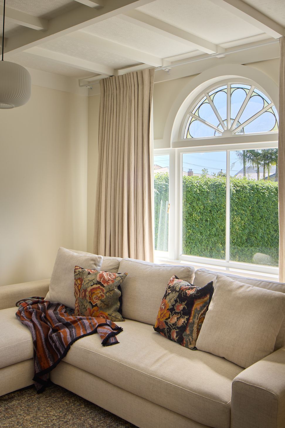 The restored front lounge celebrates the character of the original bungalow. Ornate street-facing windows with decorative fanlights, battened ceilings and linen drapery are paired with contemporary furnishings to create a timeless family living space.