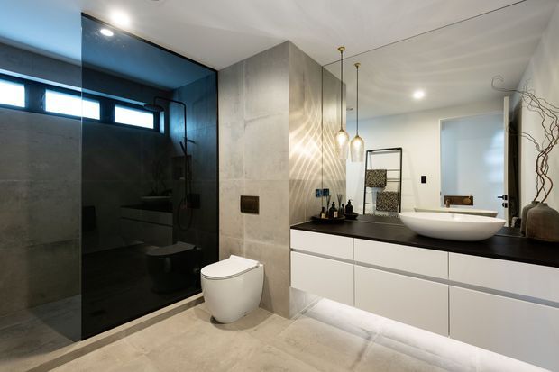 Contemporary bathroom featuring a dark glass-enclosed shower and toilet zone, a floating white vanity with a dark benchtop, a vessel basin, pendant lights, large-format neutral stone-look surfaces, and concealed under-vanity lighting.