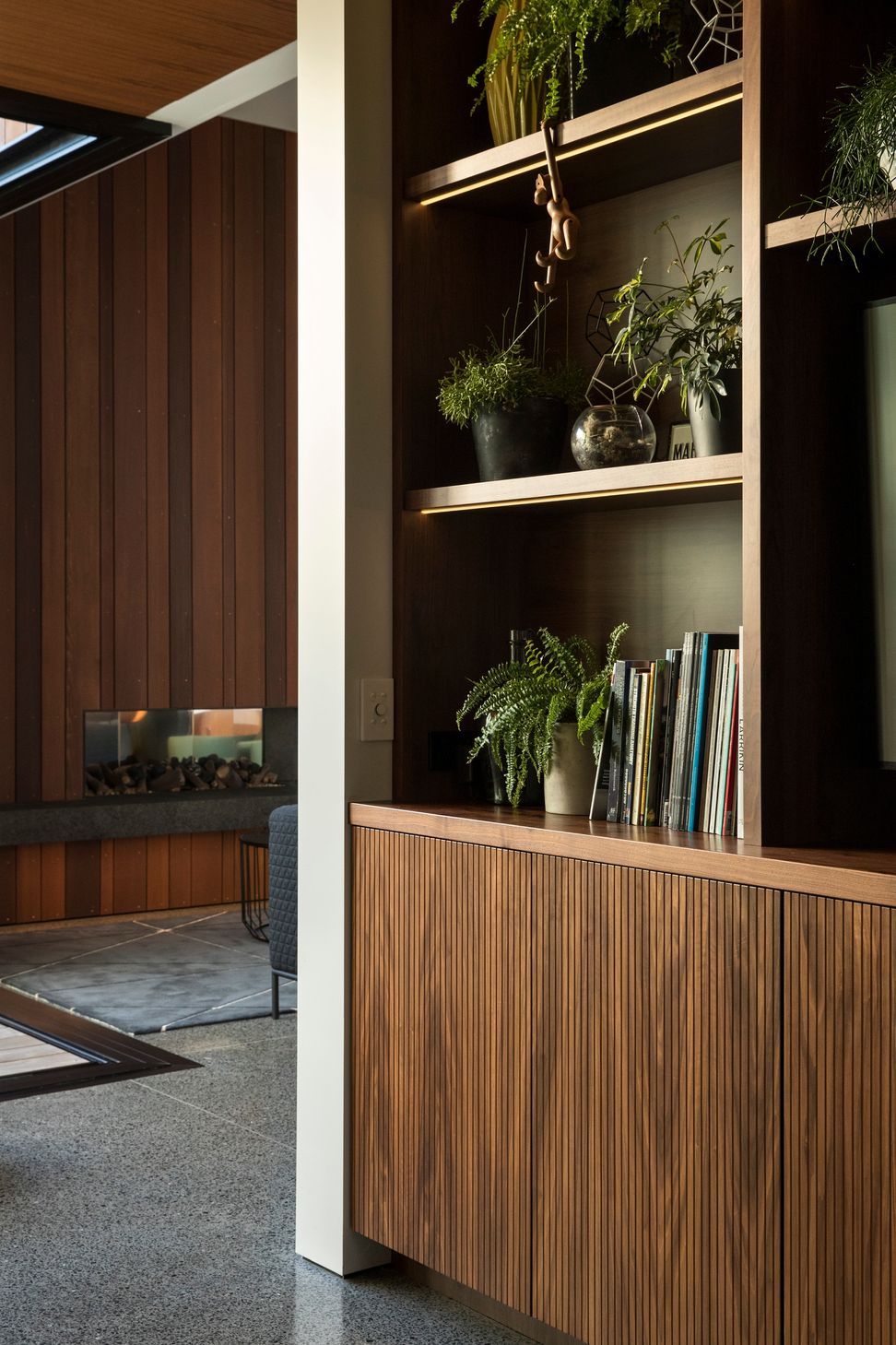 Custom walnut cabinetry provides elegant storage while complementing the warm material palette. Beyond, the cedar-lined fireplace creates a natural focal point within the living room.