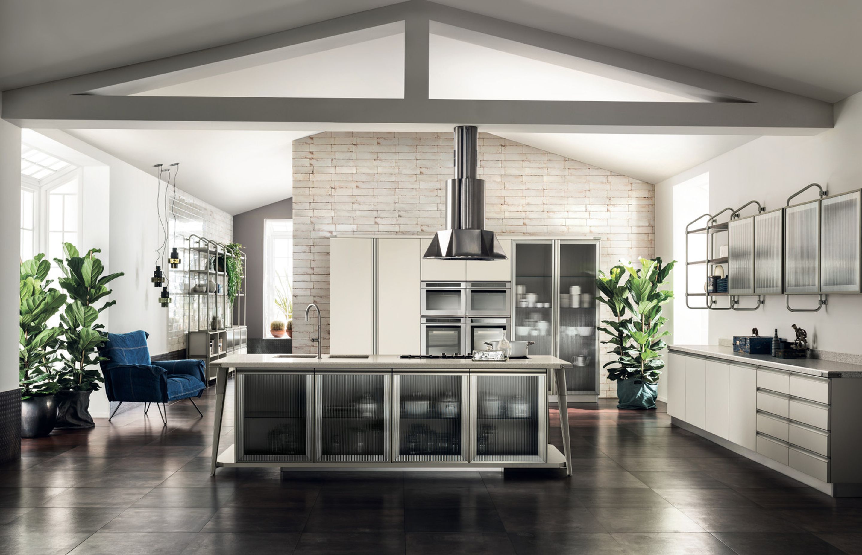 The large island appears to be suspended above the floor and the large supports, in Soft Steel finish metal, form a frame around the structures and the doors with Ribbed Glass. Both the washing area and the hob have been fitted flush with the matt finish Motley Quarz top.