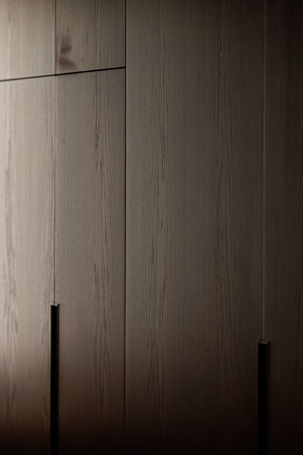 Close-up of tall, floor-to-ceiling dark wood-grain built-in cabinetry with slim black vertical pull handles. The image is tightly framed on the joinery, with subdued lighting creating a warm, moody and refined atmosphere.