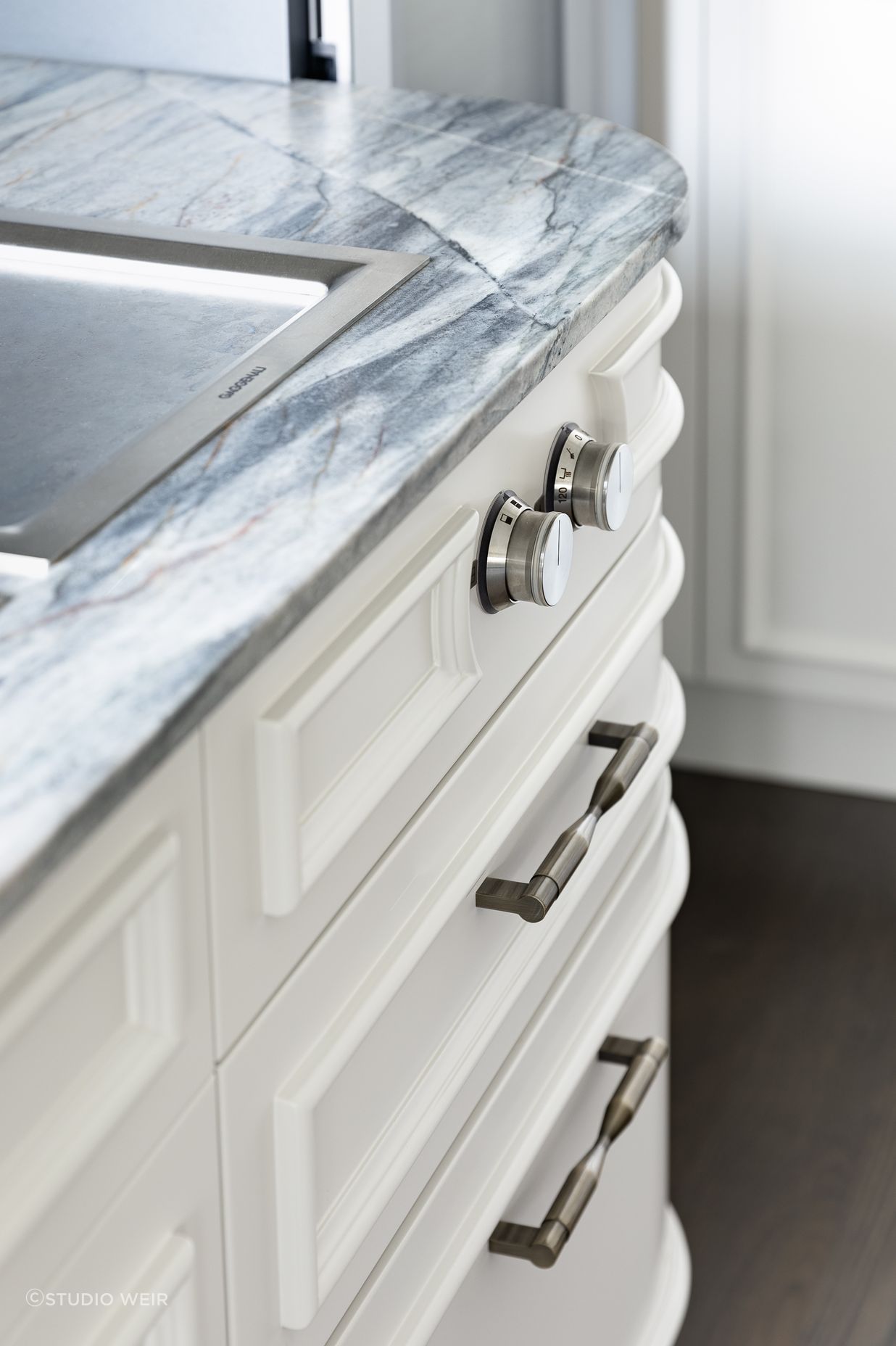 Framing the function, the round teppanyaki knobs are encircled with this moulding which then cleverly hugs the curve towards the ovens.  Echoed above on the rangehood panel, the face mouldings likewise follow the curved form softly reflecting morning light into the kitchen room; emphasising light and shadow.