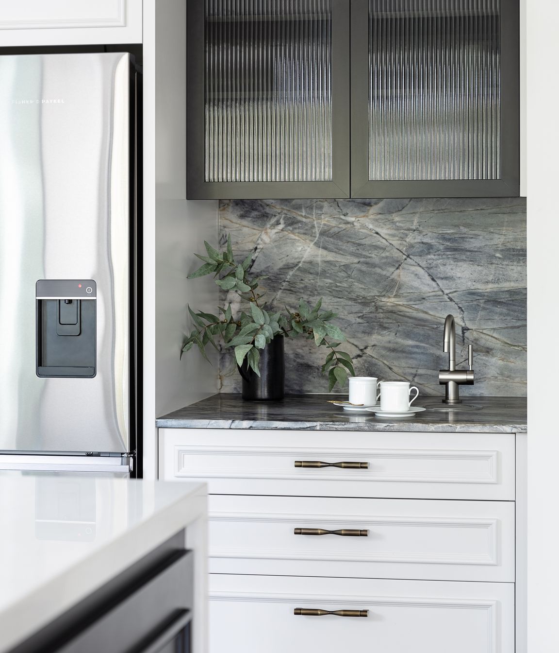The dedicated coffee zone integrates a hot water tap; another workspace for family to independently prepare. The custom black steel frame and reeded glass are mirrored here to match the table support.