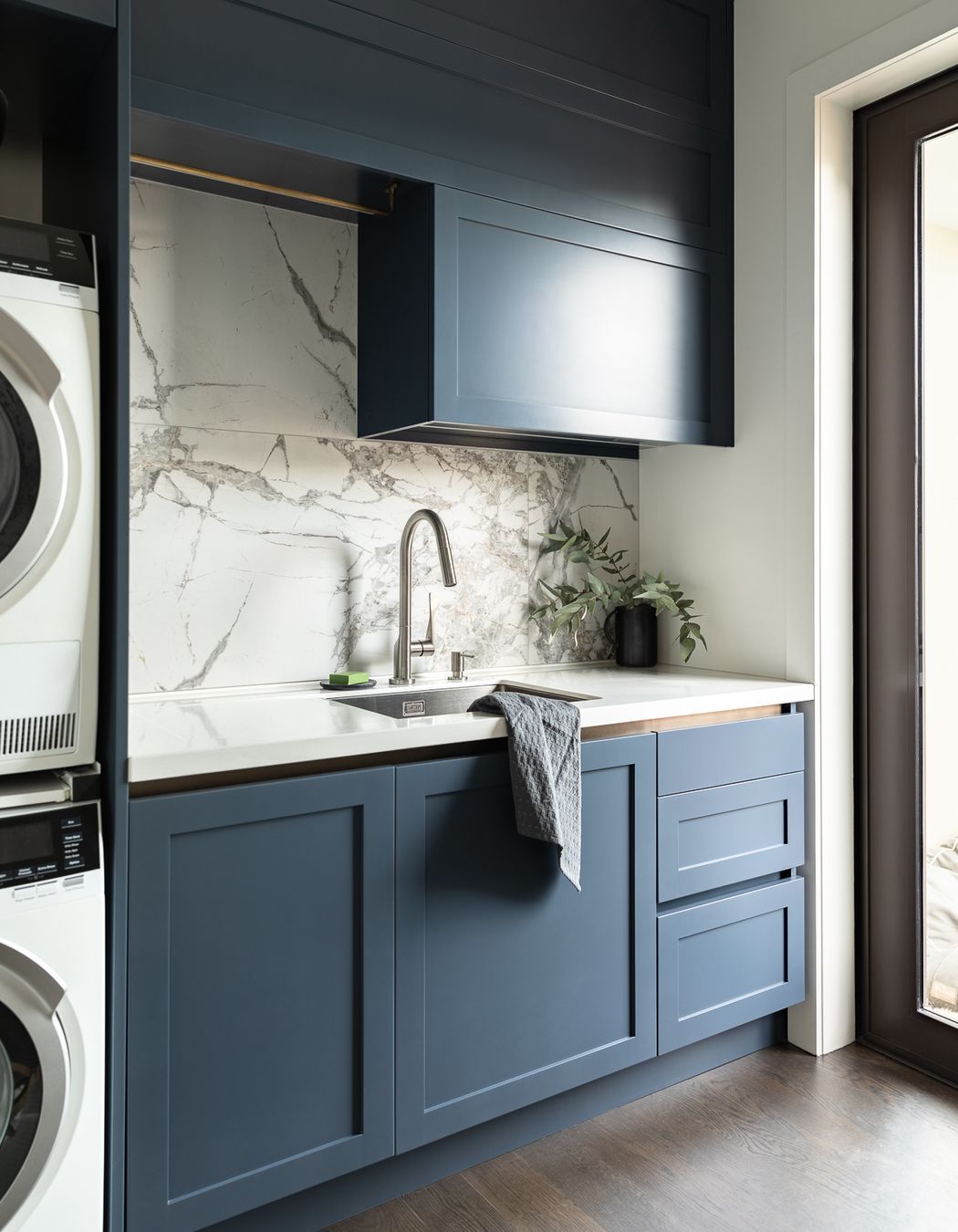 Requiring the same rigour of spatial efficiency in their compact laundry, Toni incorporated a hidden double hamper drawer, practical storage drawers and space for baskets. The navy is enriched to a bluer hue for punch, softened with a large format marble tile, subtle brass touches and an integrated drainer to the Corian work surface.