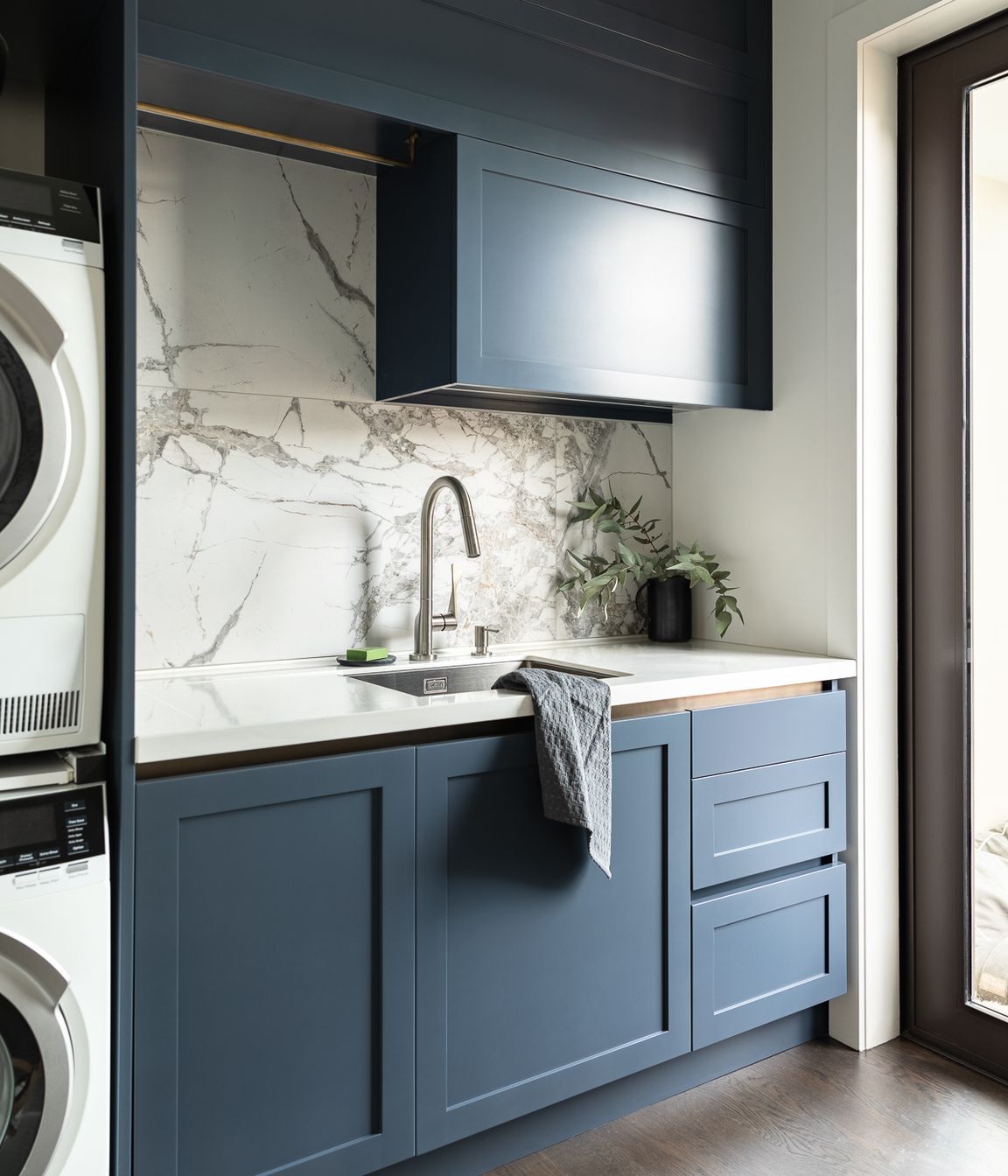 Requiring the same rigour of spatial efficiency in their compact laundry, Toni incorporated a hidden double hamper drawer, practical storage drawers and space for baskets. The navy is enriched to a bluer hue for punch, softened with a large format marble tile, subtle brass touches and an integrated drainer to the Corian work surface.