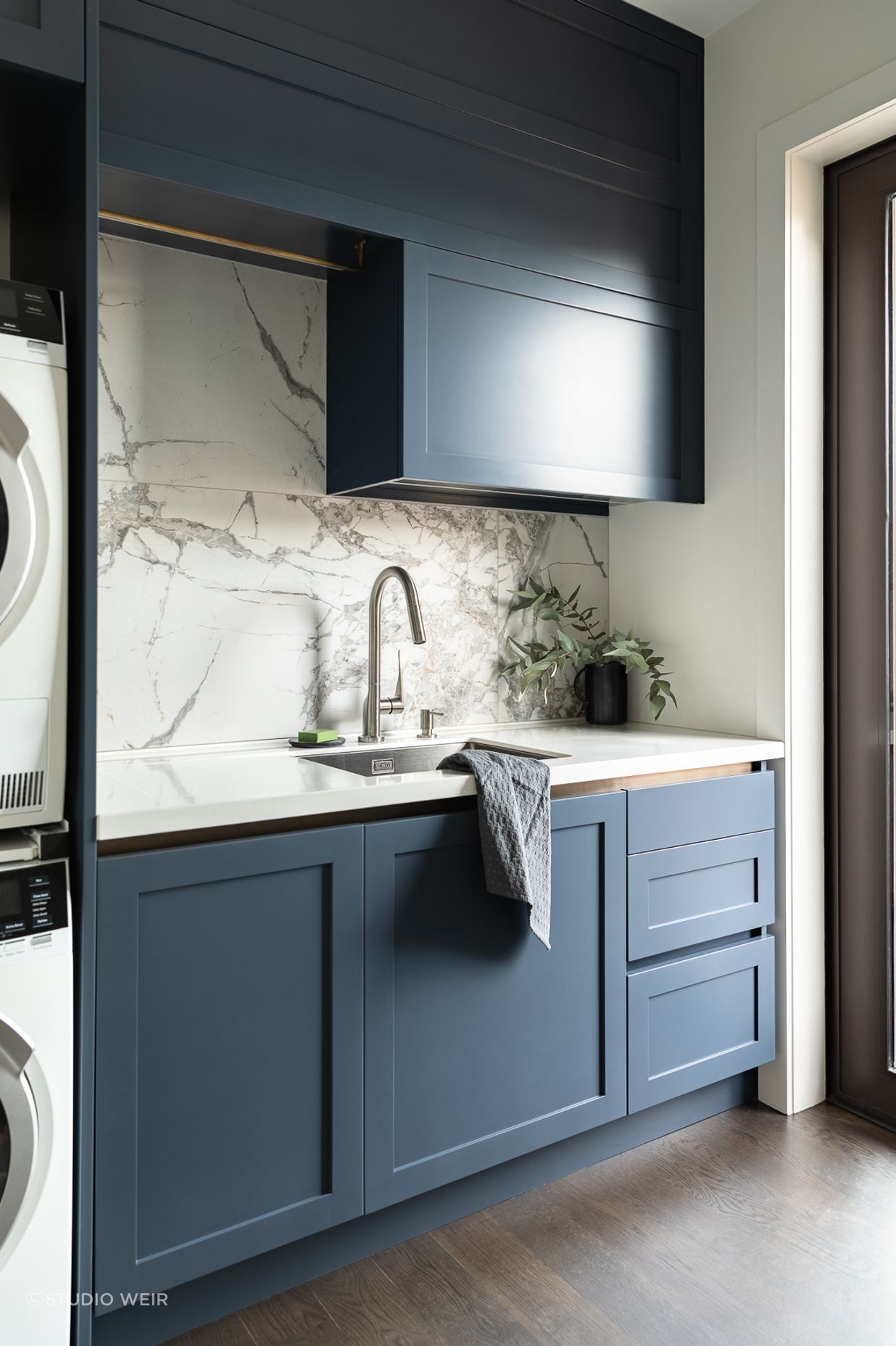 Requiring the same rigour of spatial efficiency in their compact laundry, Toni incorporated a hidden double hamper drawer, practical storage drawers and space for baskets. The navy is enriched to a bluer hue for punch, softened with a large format marble tile, subtle brass touches and an integrated drainer to the Corian work surface.