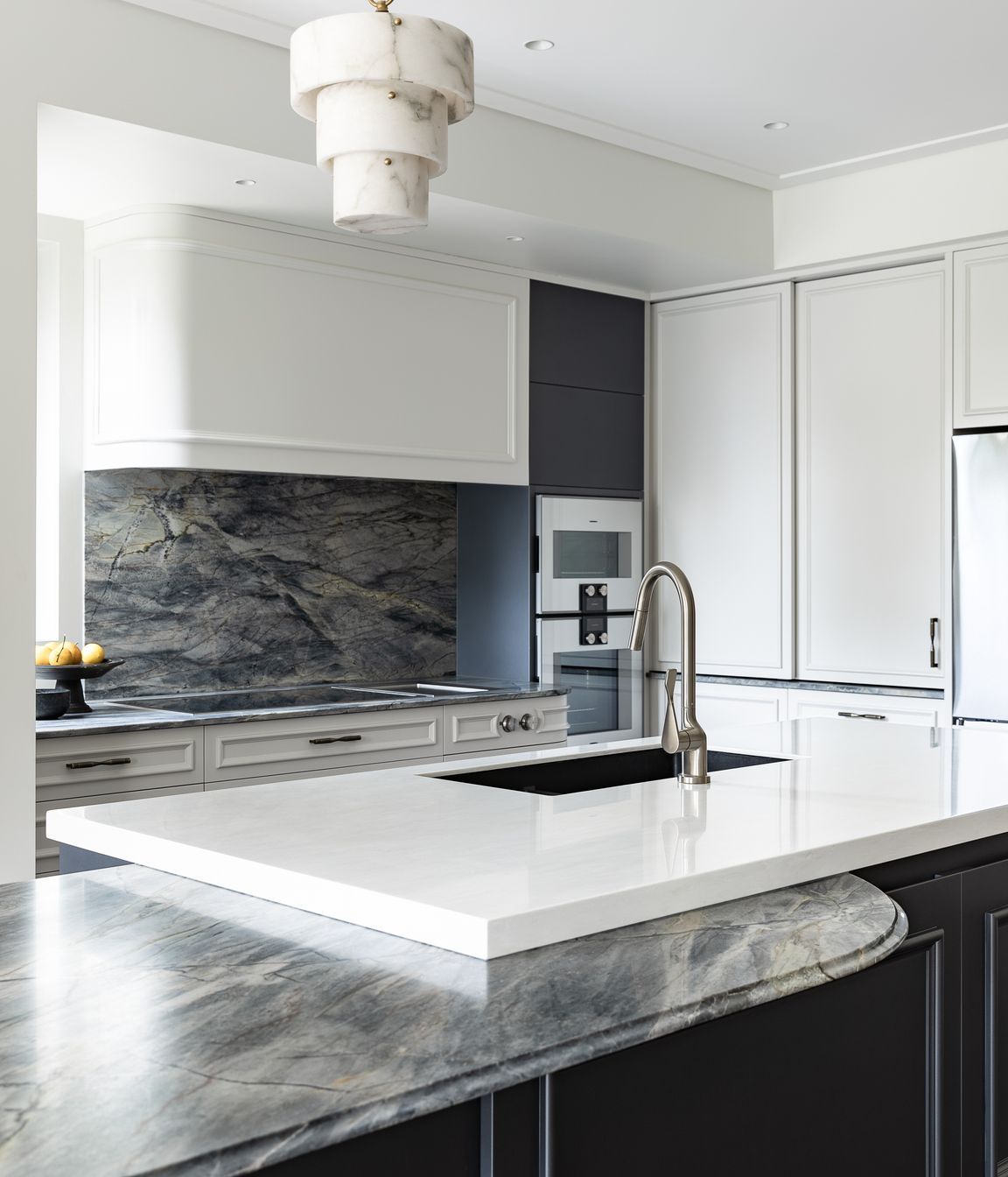 Toni seamlessly integrated Neoclassic touches and cohesive design detailing to create a welcoming exciting space, beautifully designed for entertaining and everyday family life.   The island incorporates large double sinks and bins, with the hob bench behind curving around to meet an oven tower set flush with panels above, making use of the old pantry recess.