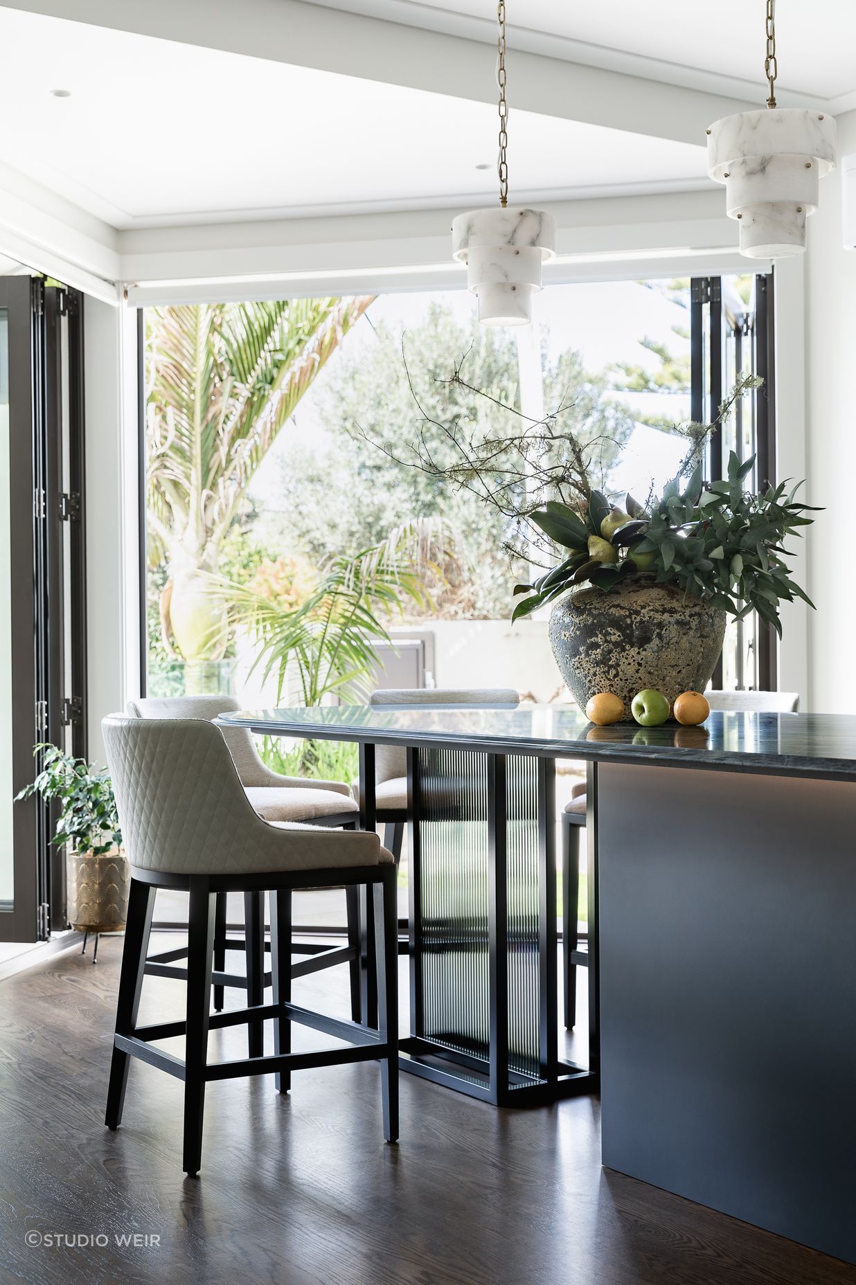 Supporting the table-island, Toni designed a custom black steel frame with back-to-back reeded glass insets, configured for safety and removability and sheathed in a smoke film for visual interest.  Integrated bead lighting below the table follows the curve.