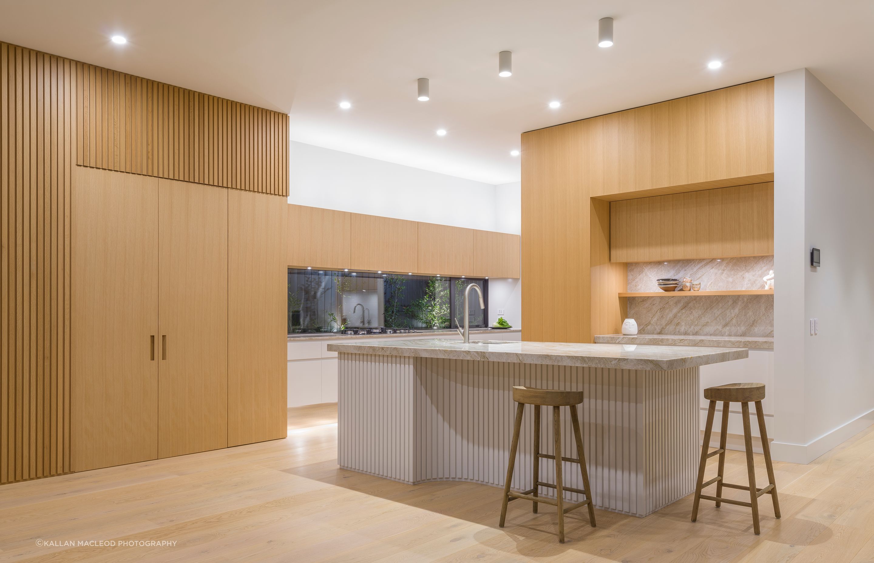 In true mid-century style, a dramatic 4.2 metre elongated window is configured as a key form. Long oak cupboards above and white drawers below repeat the same horizontal rhythm and proportions, emphasised by layering discreet LED lighting to each of the three levels.  Designed in 2019 before battened sheets became mainstream, each ‘pleat’ is carefully predetermined and dimensioned to read as evenly spaced even within the internal curvature. Like a perfectly hemmed garment, the battens just lightly skirt the floor.