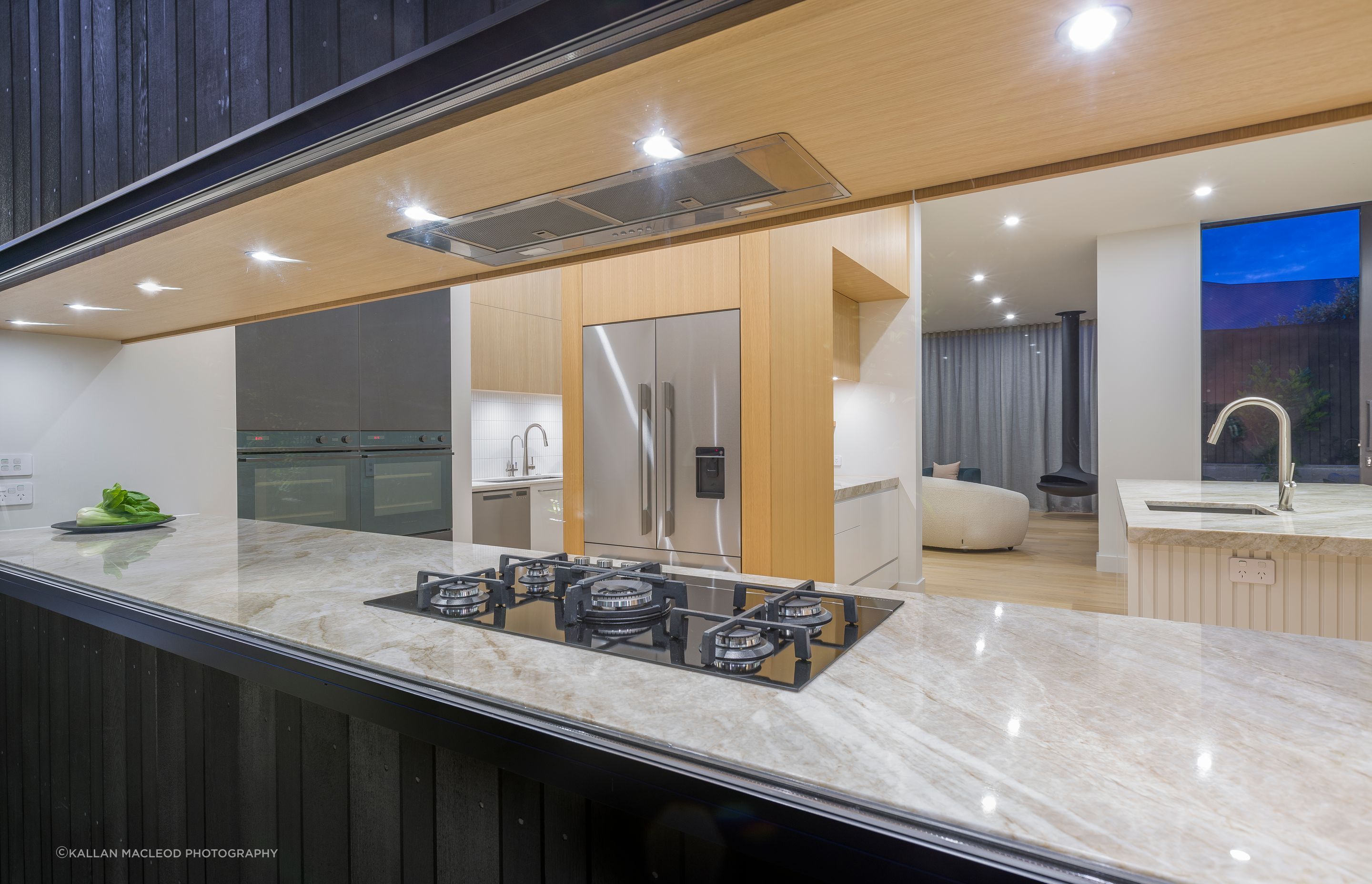This view from outside reveals the scullery beyond and the attention to fine detailing of each material to the glass frame; a careful collaboration of several trades at site.  Wanting appliances hidden yet intuitively accessible, the fridge and ovens are tucked around the corner for guests' first-impression of elegance.
