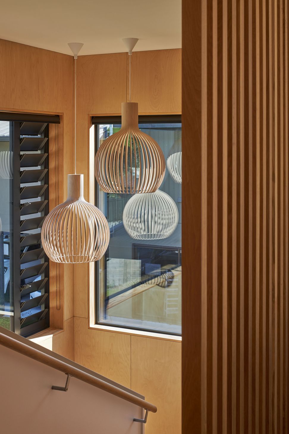 The stairwell brings together natural materials and filtered light to create a warm, inviting transition between levels. Birch plywood walls and an oak screen introduce texture and rhythm, while sculptural timber pendant lights draw the eye upward, transforming the circulation space into a quiet architectural feature within the home.