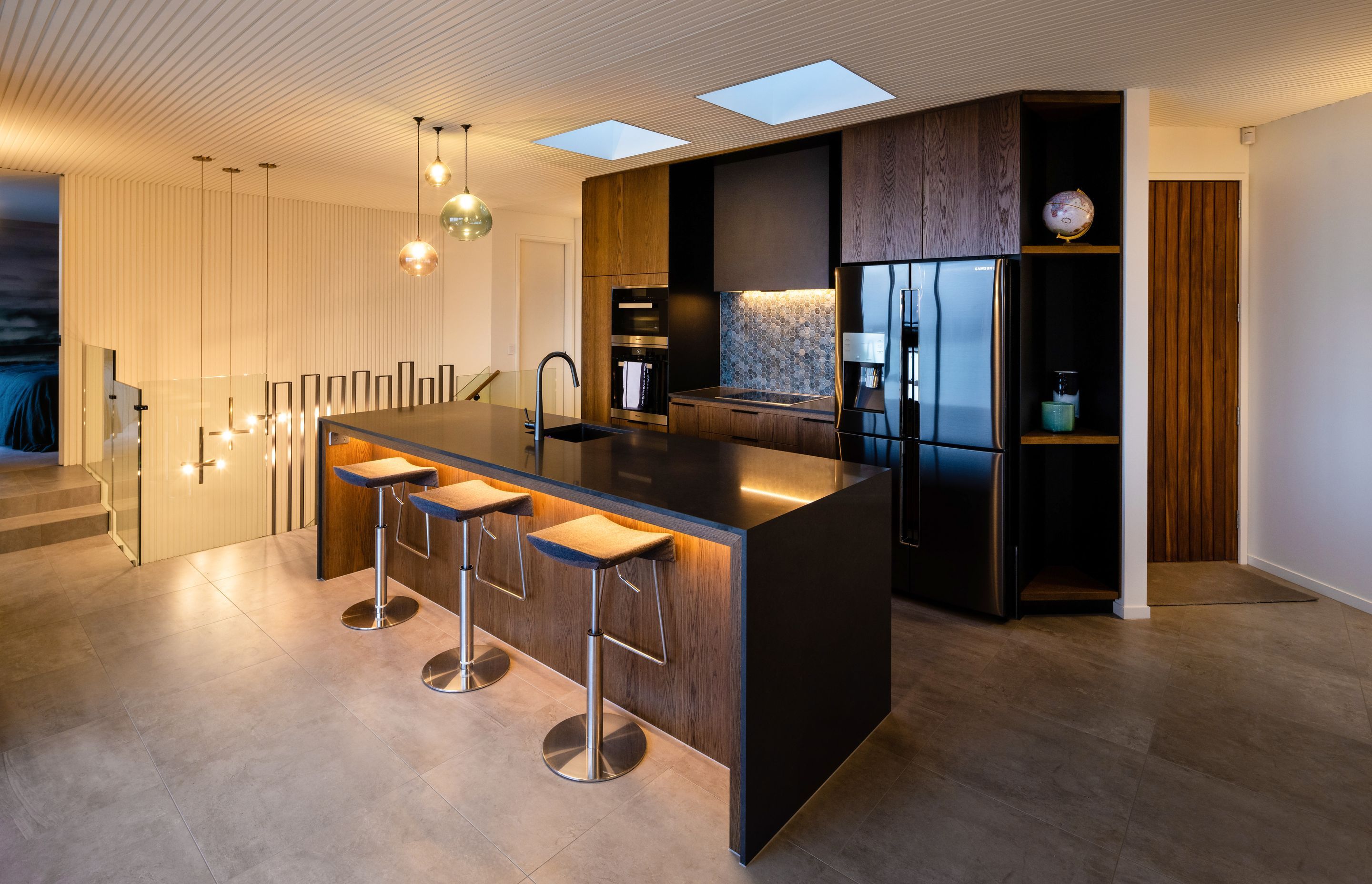 The kitchen features rich timber laminated cabinetry and a routed ceiling surface that leads the eye across the room and down the stairwell.