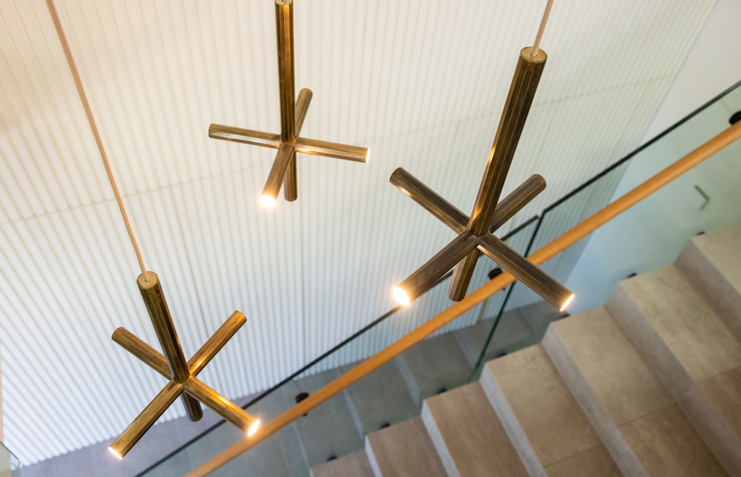 Feature brass pendant lights light up the stairwell and add warmth to the white and grey interior palette.