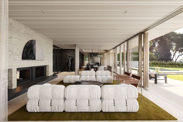 A spacious, refined modern living room with a long linear layout and floor-to-ceiling glazing along one side. The room features a large cream modular sofa arrangement, a dark built-in fireplace wall with pale textured stone or concrete finish, a low round coffee table, a sculptural wall artwork, and a dining area beyond. The glazed side opens visually to a terrace and swimming pool, bringing in abundant natural light. The ceiling has continuous narrow linear panelling, and slender dark-framed glazing creates a strong indoor-outdoor connection.